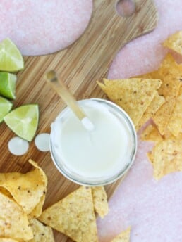 4 Ingredient Greek Yogurt Lime Crema in a white bowl on a butcher block with chips and limes on the side