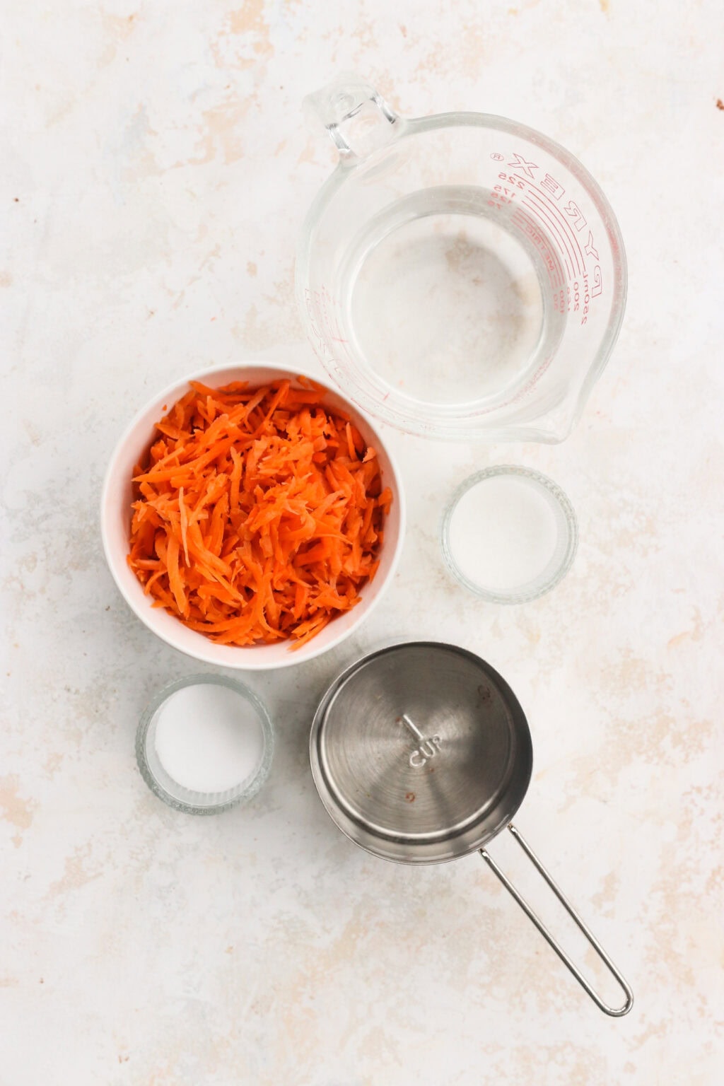 Ingredients for quick pickled shredded carrots, including shredded carrots, salt, sugar, vinegar, and hot water