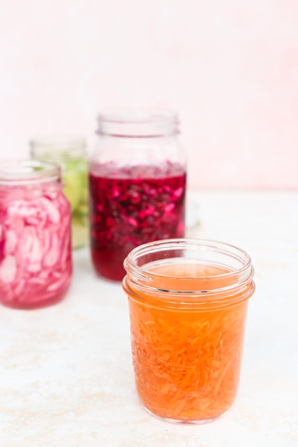 Quick pickled shredded carrots, red cabbage, avocados, and red onions in four glass jars