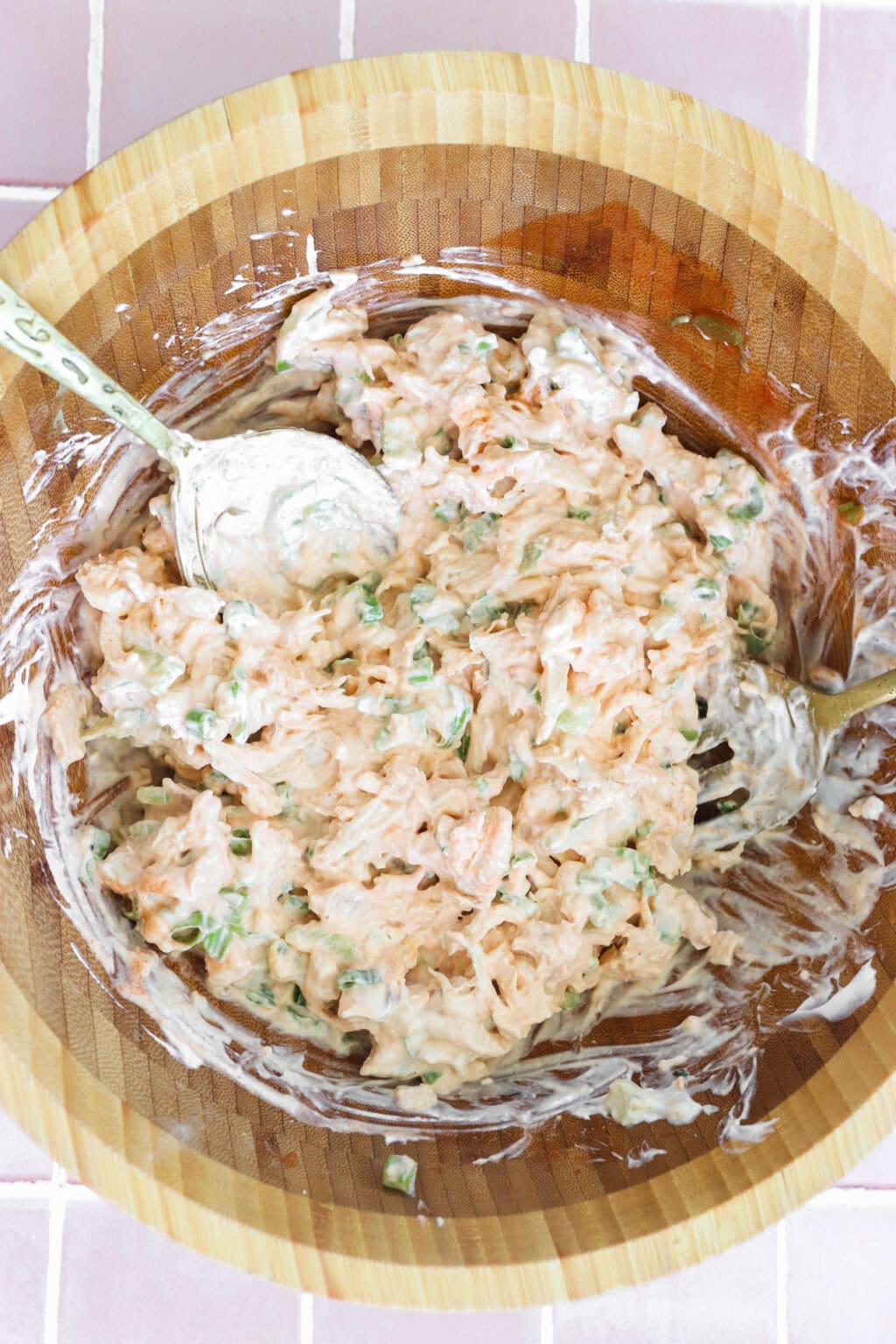 Ingredients for Quick Buffalo Chicken Salad with Greek Yogurt mixed in a medium wooden bowl including cooked shredded chicken, Greek yogurt, mayo, Frank's Red Hot Original Sauce, garlic powder, green onions, blue cheese, pepper