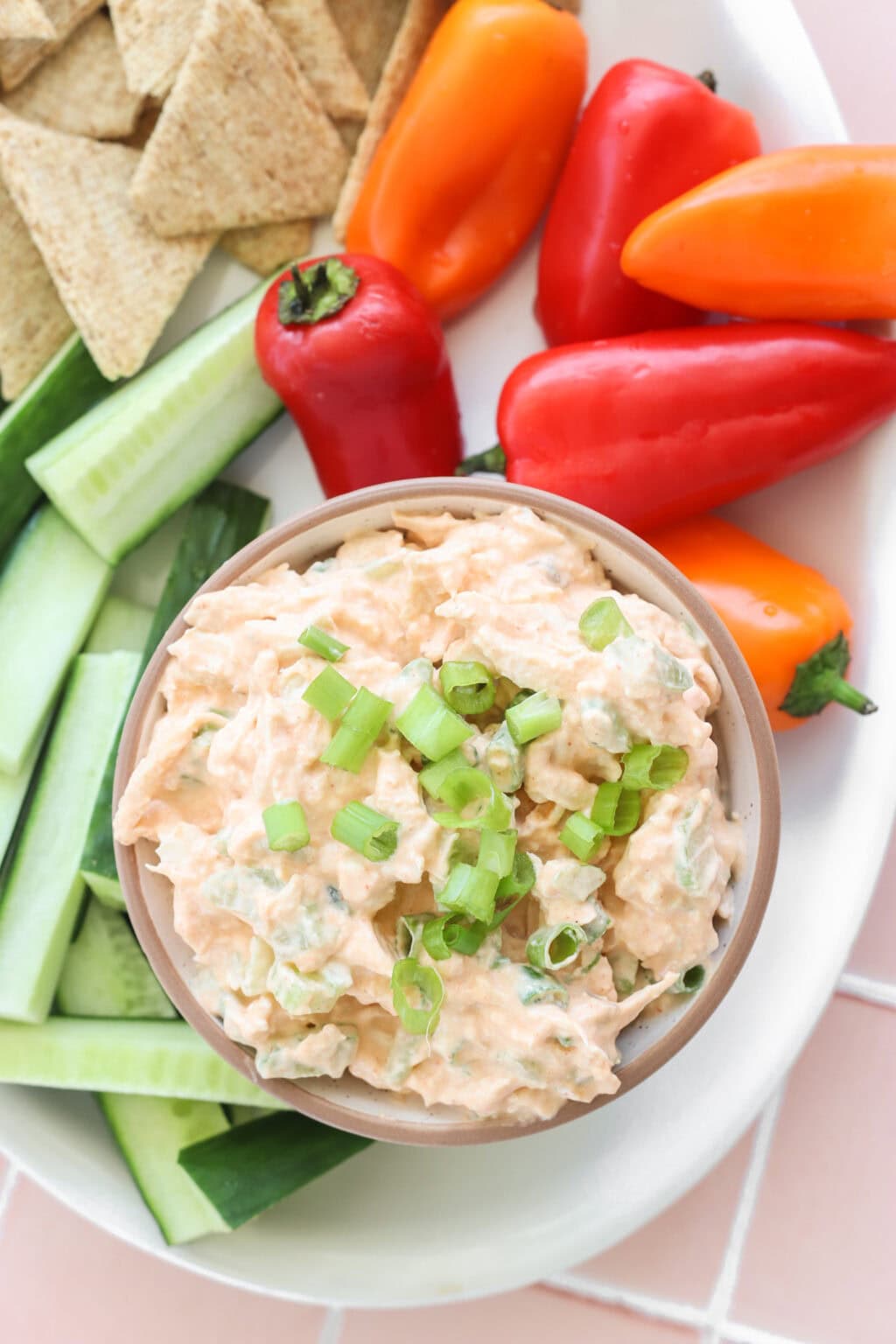 Quick Buffalo Chicken Salad with Greek Yogurt in a glass bowl on a white serving tray with celery, peppers, and crackers on the side
