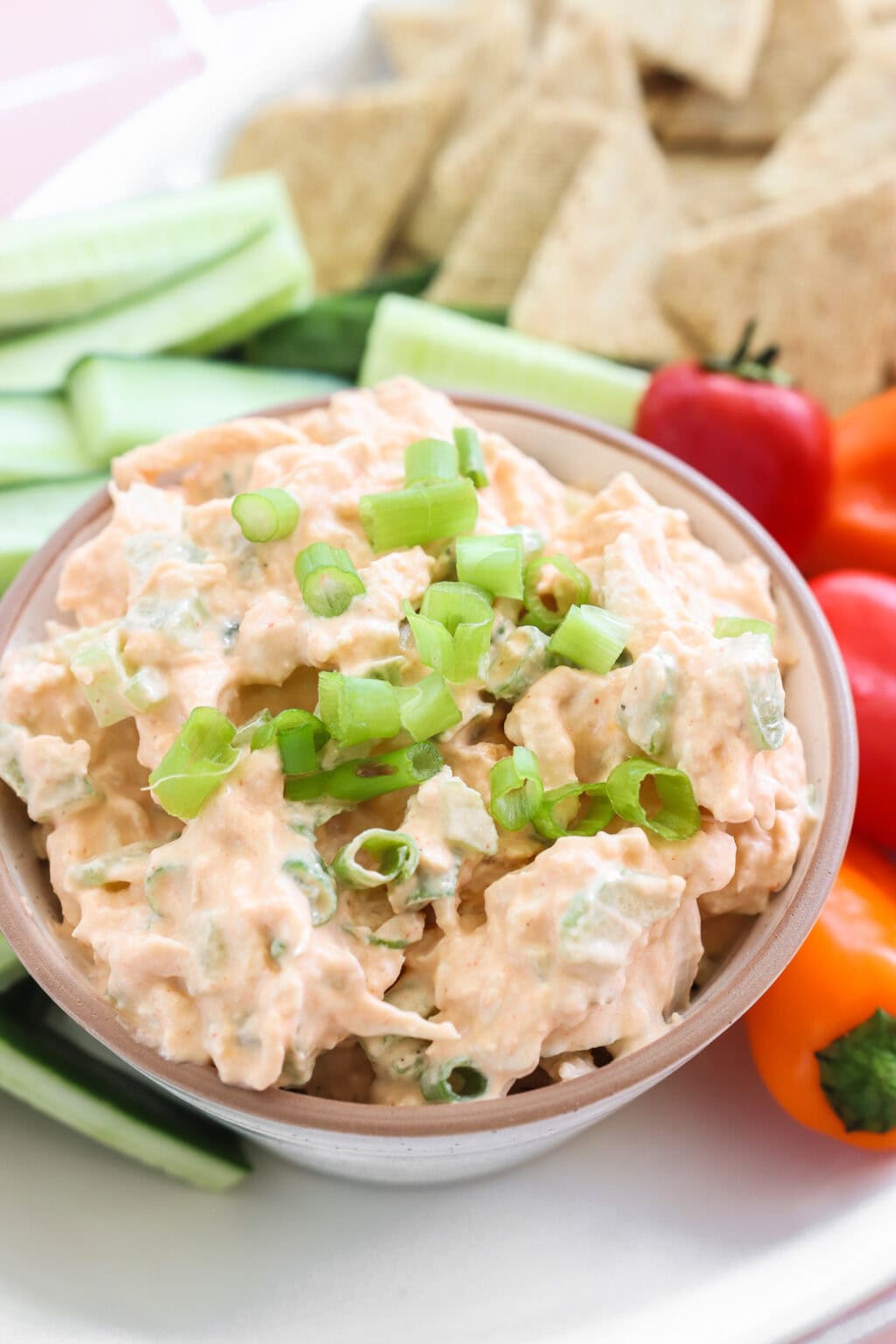 Quick Buffalo Chicken Salad with Greek Yogurt in a glass bowl on a white serving tray with celery, peppers, and crackers on the side