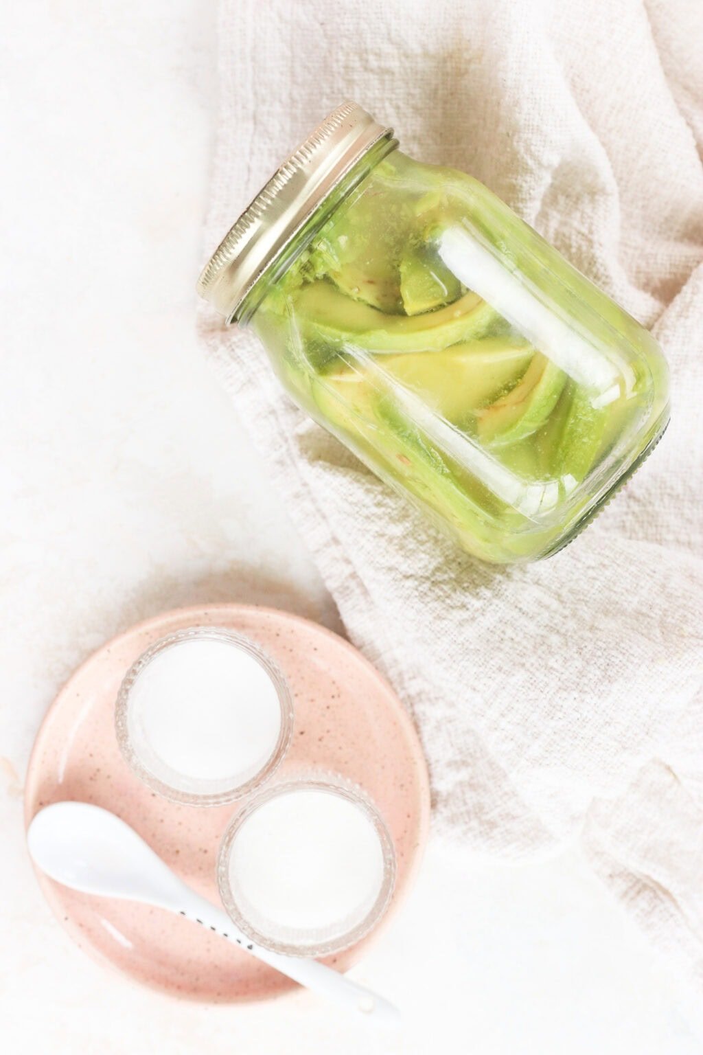 Quick pickled avocados in a glass jar with a pink plate beside it