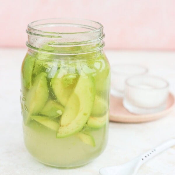 Quick pickled avocados in a glass jar with a pink plate beside it