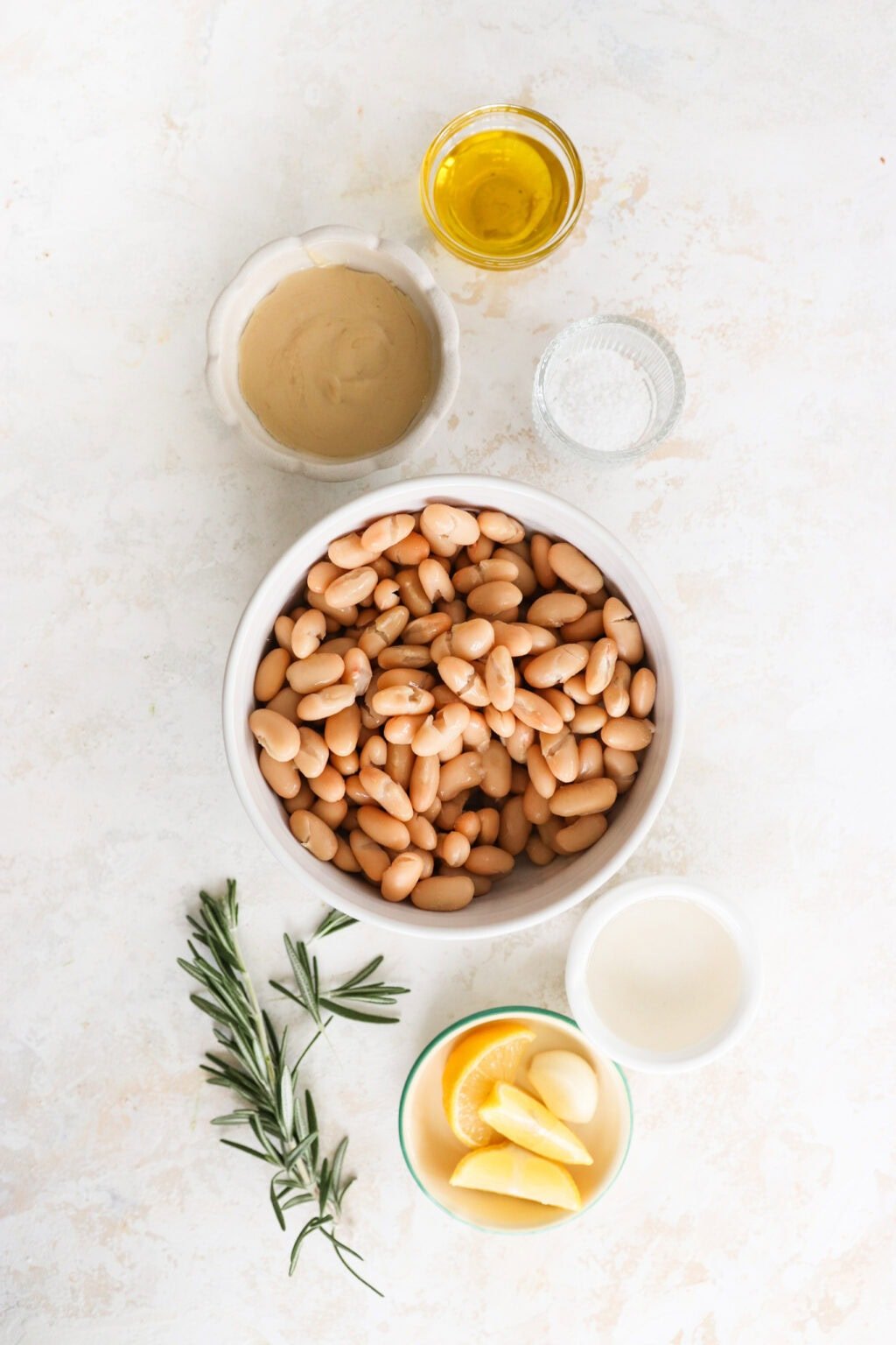 Ingredients for Super Creamy Vegan White Bean Dip with Cashews in small glass bowls, including cannellini beans, cashews, extra virgin olive oil, salt, lemon juice