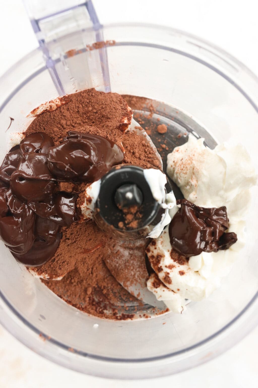 Ingredients for Whipped Greek Yogurt Chocolate Mousse unblended in a food processor, including chocolate chips, Greek yogurt, cacao and salt