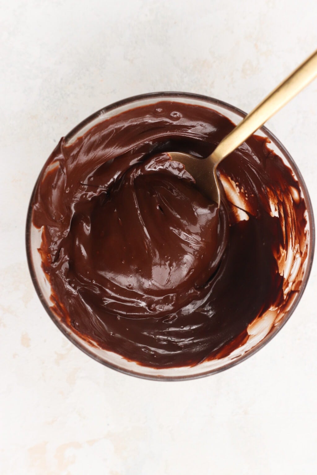 Melted chocolate chips in a glass bowl with a gold spoon to use in the Whipped Greek Yogurt Chocolate Mousse