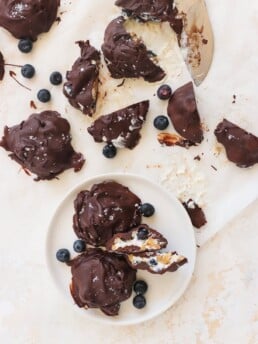 A counter scattered with Frozen Blueberry Greek Yogurt Clusters with some loose blueberries and a white plate with two clusters on it