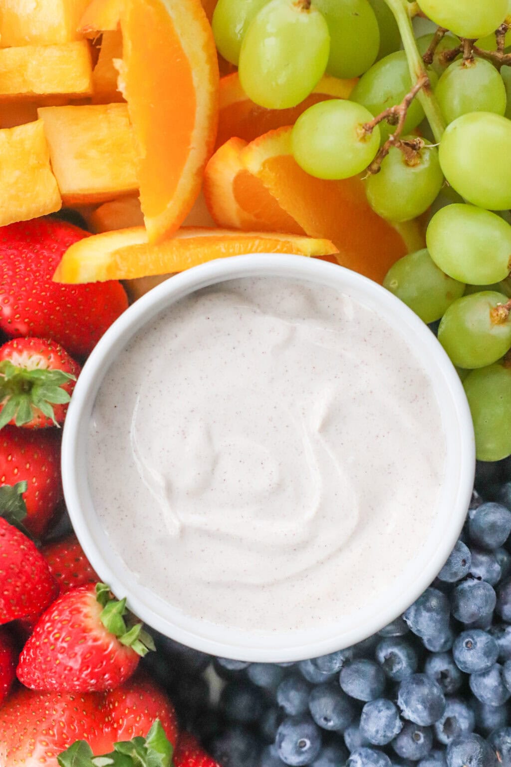 The Best Honey-Cinnamon Greek Yogurt Fruit Dip (easy high protein snack) in a white bowl on top of a tray filled with fruit