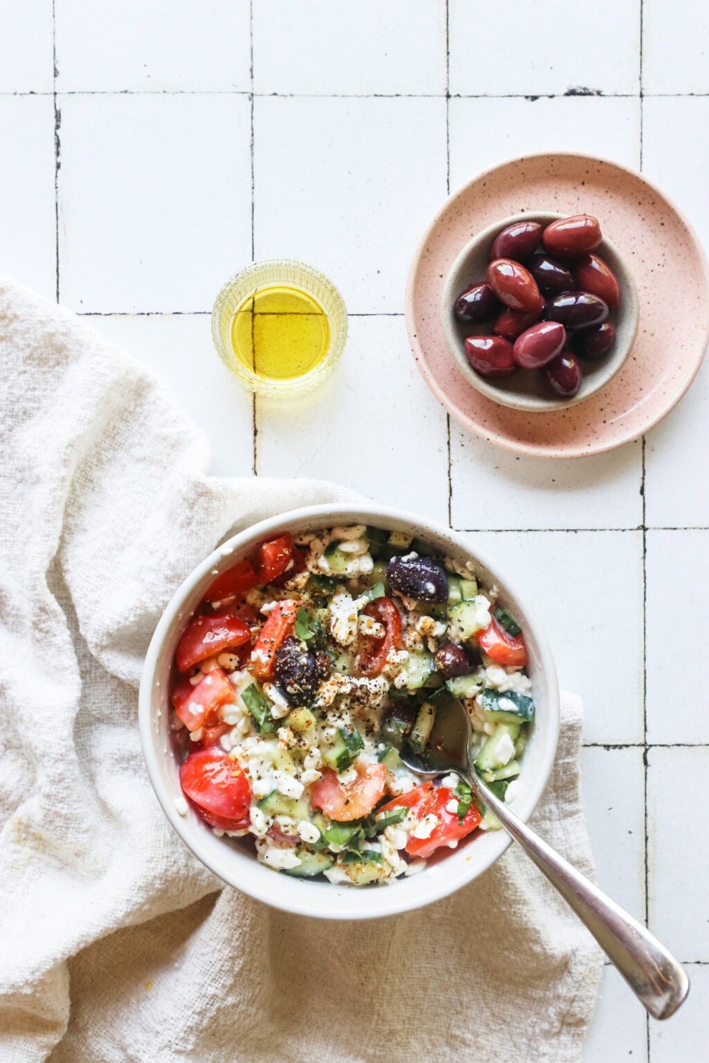 Easy Greek-Inspired Cottage Cheese Salad in a white bowl with a pink plate of olives on the side