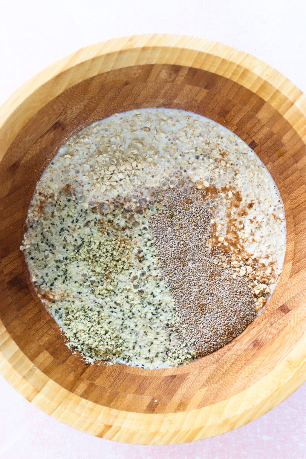 Ingredients for Grab-and-Go Strawberry Overnight Oats unmixed in a wood bowl, including rolled oats, milk, maple syrup, chia seeds, hemp hearts, ground cinnamon, salt, strawberries, vanilla Greek yogurt