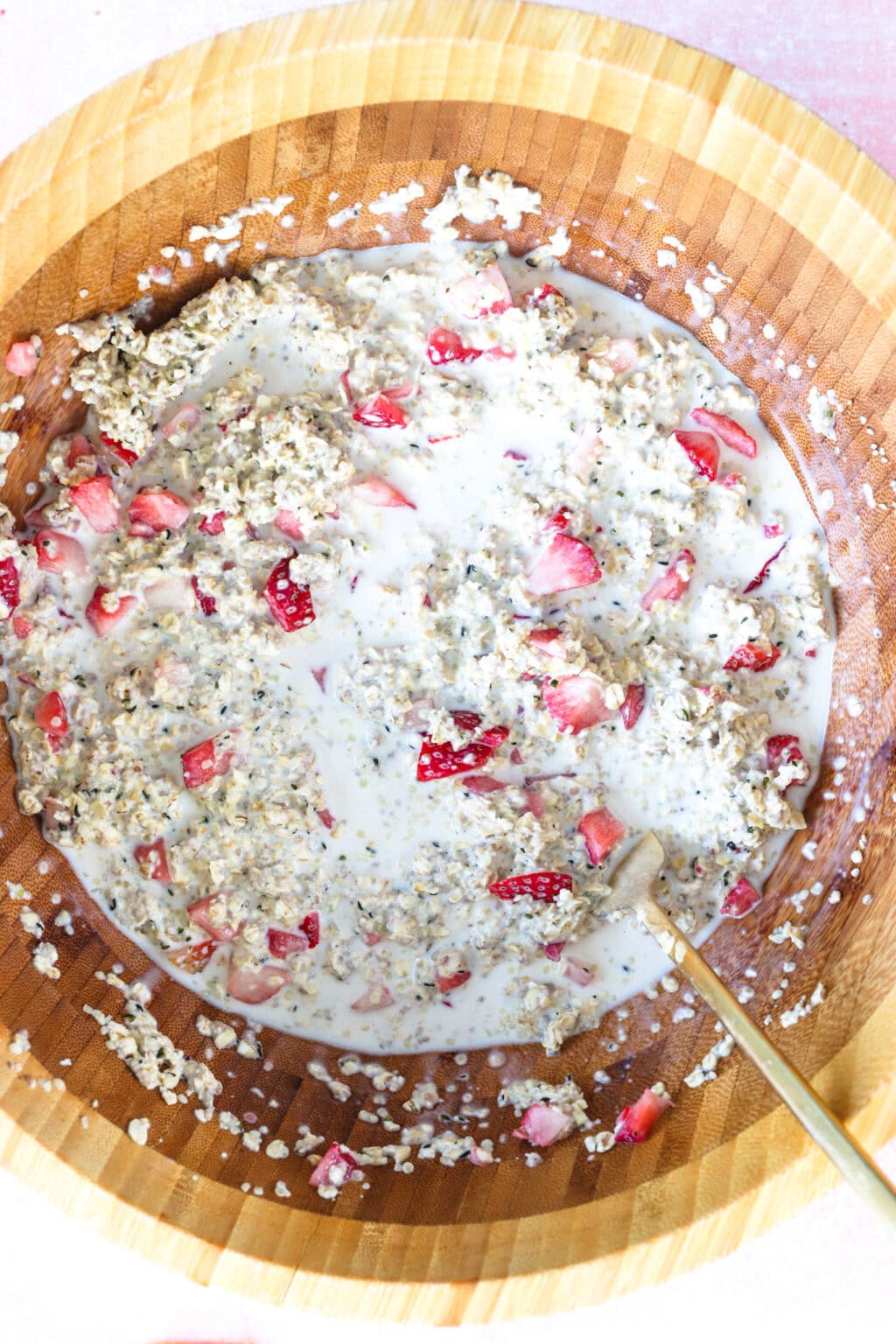 Ingredients for Grab-and-Go Strawberry Overnight Oats mixed in a wood bowl, including rolled oats, milk, maple syrup, chia seeds, hemp hearts, ground cinnamon, salt, strawberries, vanilla Greek yogurt
