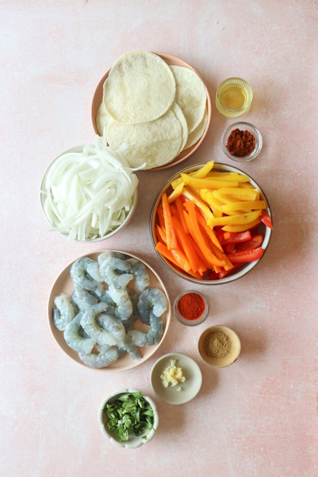 Ingredients for 30 Minute Sheetpan Shrimp Fajitas in small bowls, including shrimp, avocado oil, lime juice, chili powder, smoked paprika, cumin, honey, salt, black pepper, garlic, bell peppers, onion, flour tortillas