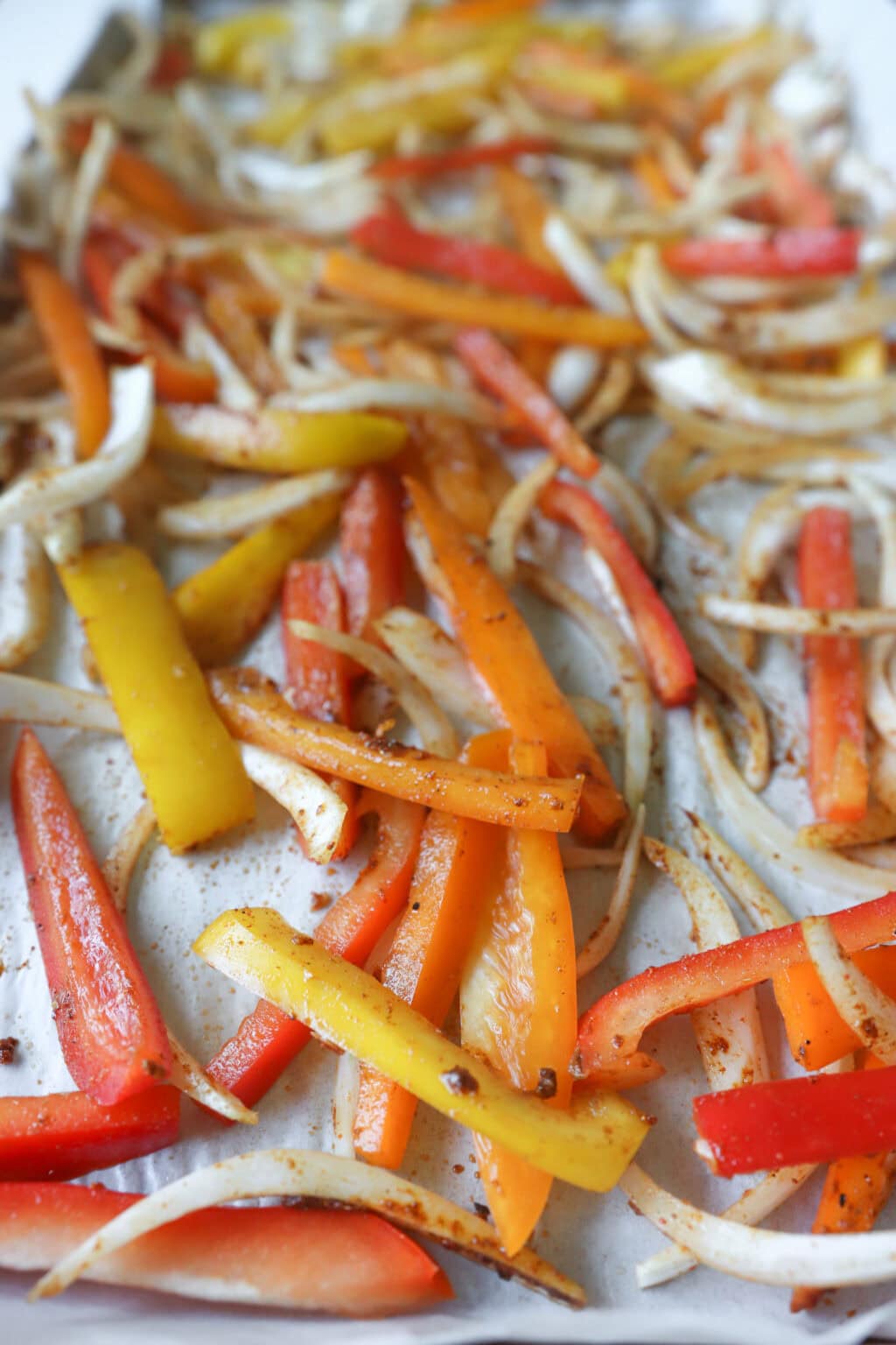 Sliced peppers and onions on a sheetpan with parchment paper for 30 Minute Sheetpan Shrimp Fajitas