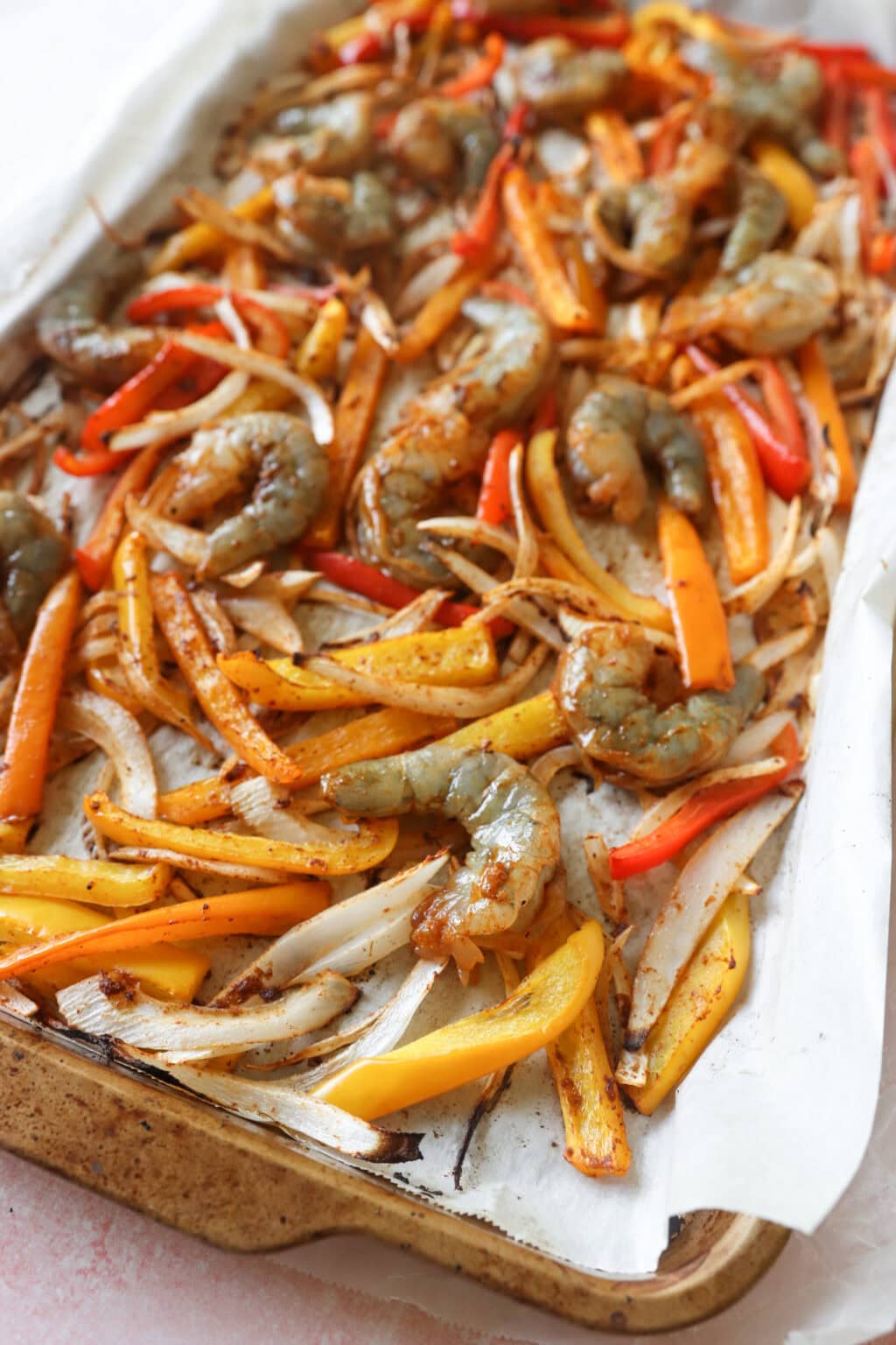 Sliced peppers, shrimp, and onions uncooked on a sheetpan with parchment paper for 30 Minute Sheetpan Shrimp Fajitas