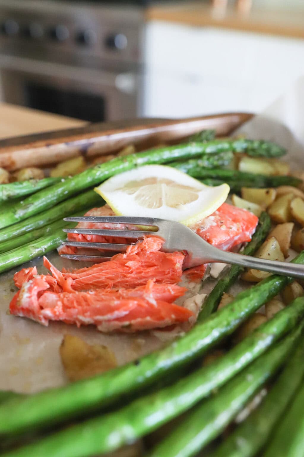 Lemon, salmon, asparagus and diced potatoes on a sheet pan with parchment paper with a fork in the salmon