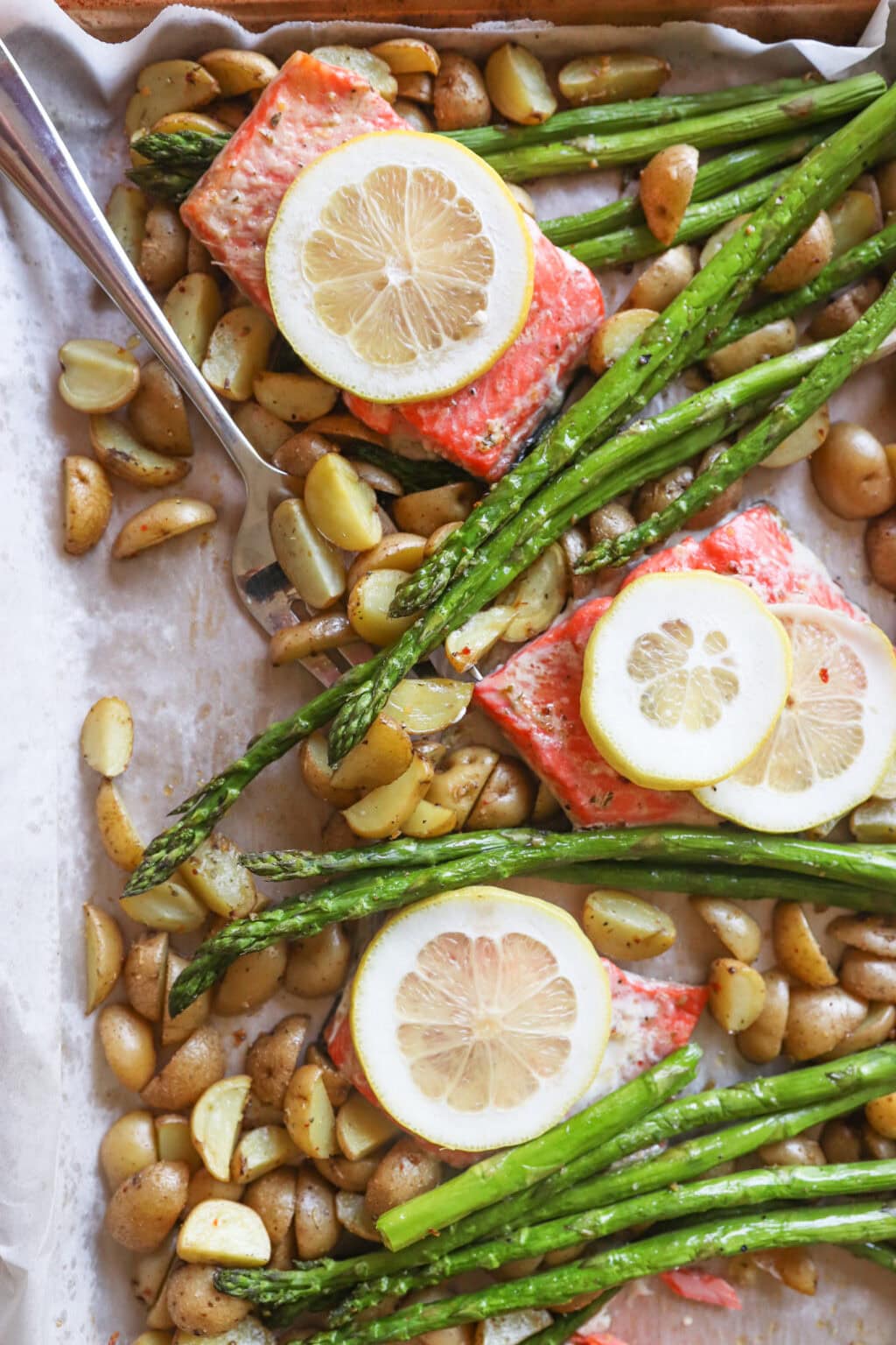 Lemon, salmon, asparagus and diced potatoes on a sheet pan with parchment paper