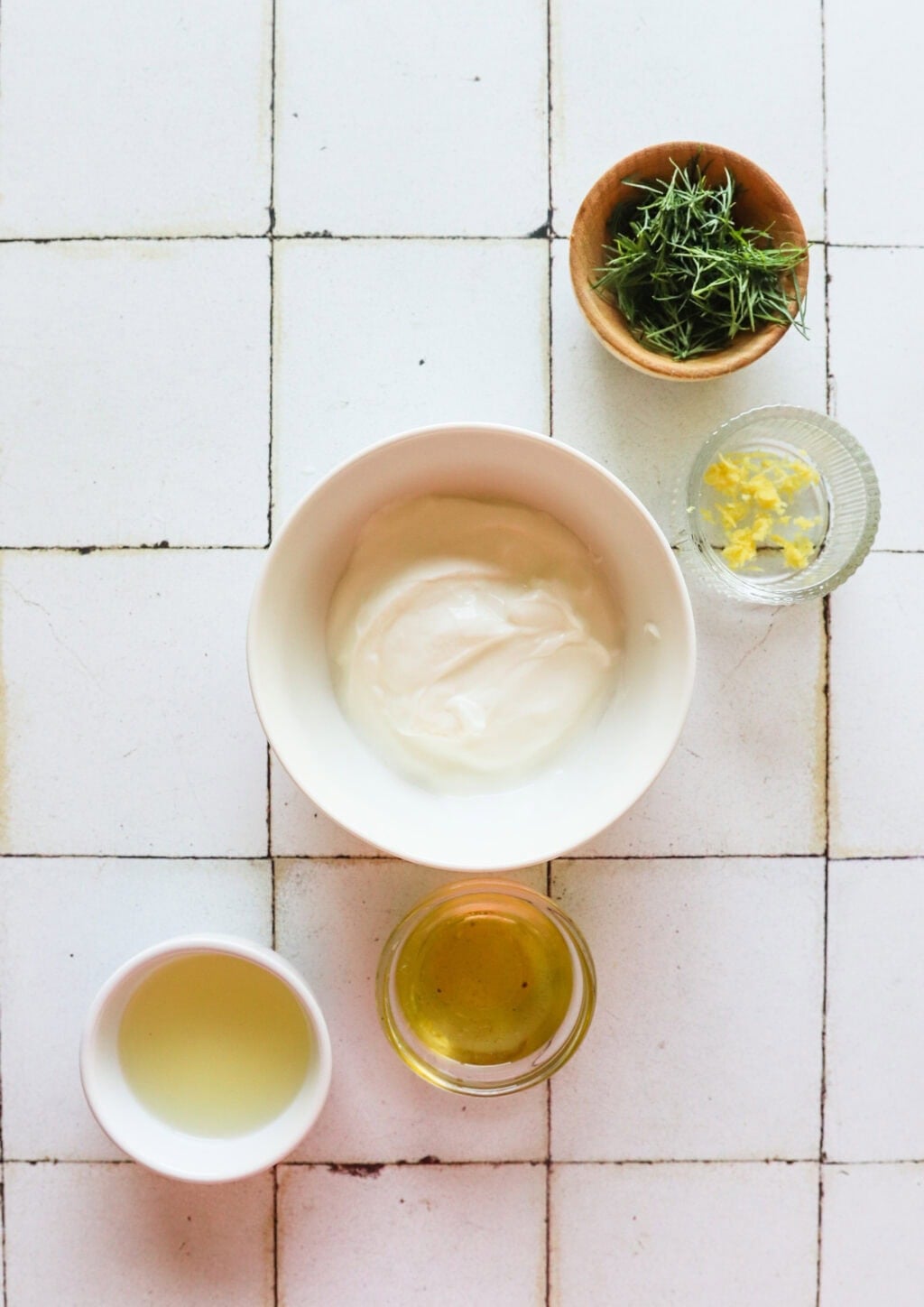 Ingredients for 5-Minute Lemon Dill Sauce with Greek Yogurt in white bowls, including Greek yogurt, olive oil, lemon zest, lemon juice, fresh dill
