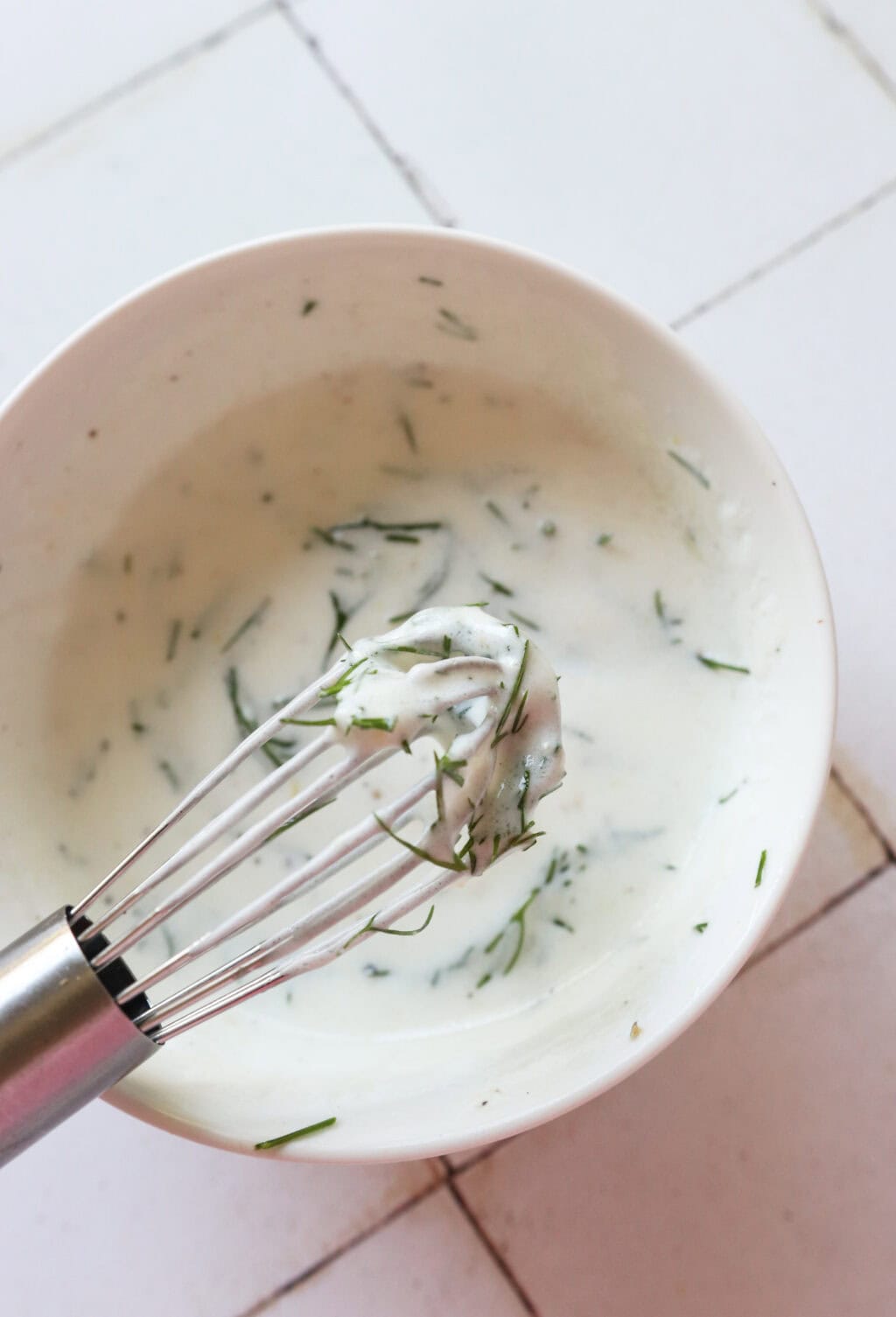 Ingredients for 5-Minute Lemon Dill Sauce with Greek Yogurt mixed in a white bowl, including Greek yogurt, olive oil, lemon zest, lemon juice, fresh dill