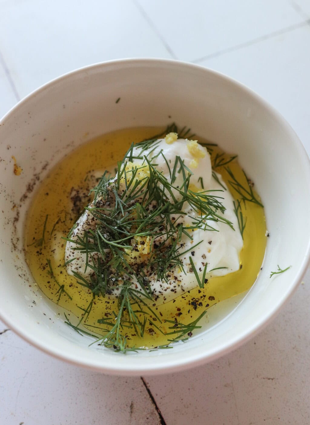 Ingredients for 5-Minute Lemon Dill Sauce with Greek Yogurt unmixed in a white bowl, including Greek yogurt, olive oil, lemon zest, lemon juice, fresh dill