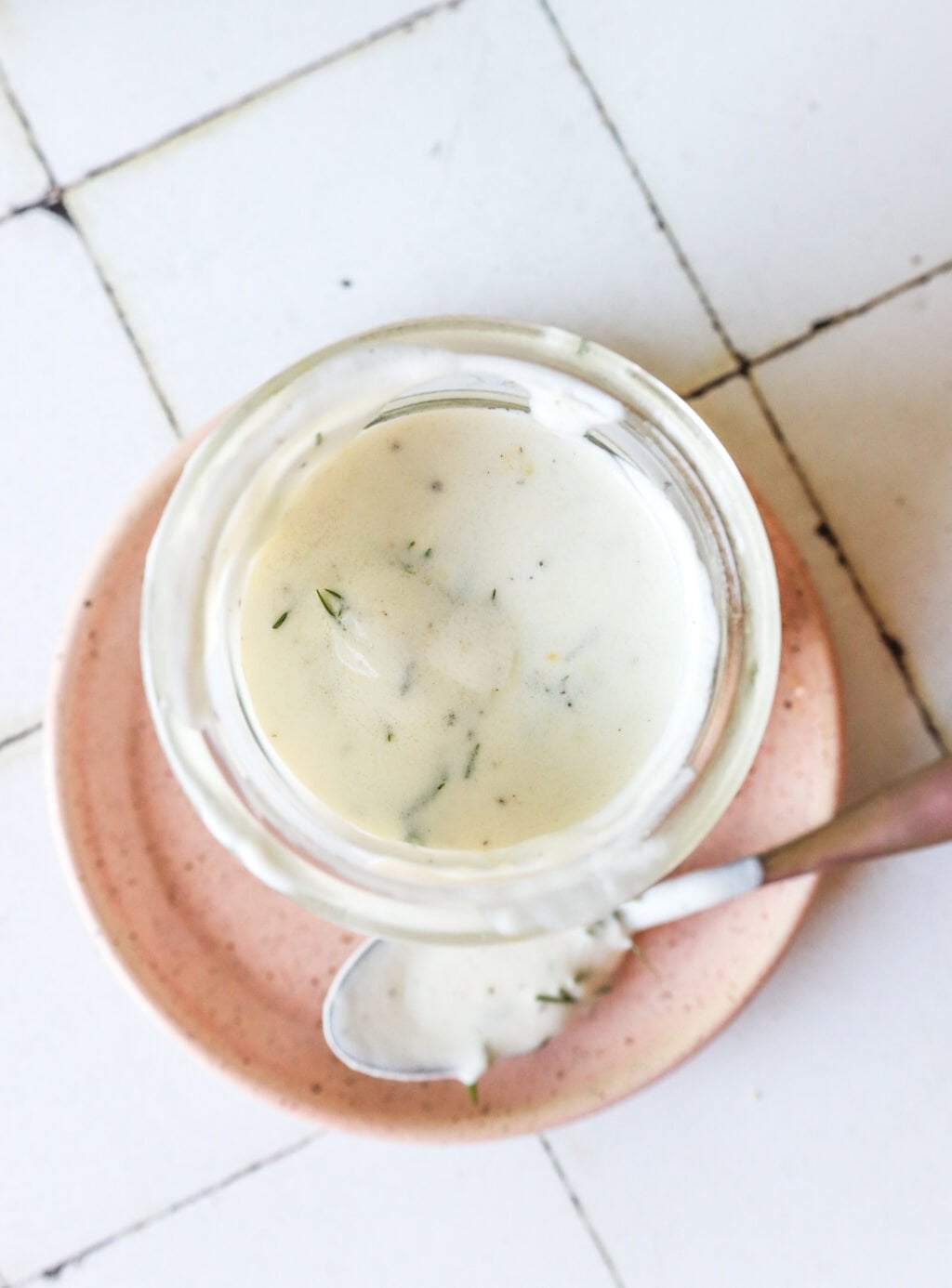 5-Minute Lemon Dill Sauce with Greek Yogurt in a glass jar on a pink plate with a spoon on the side