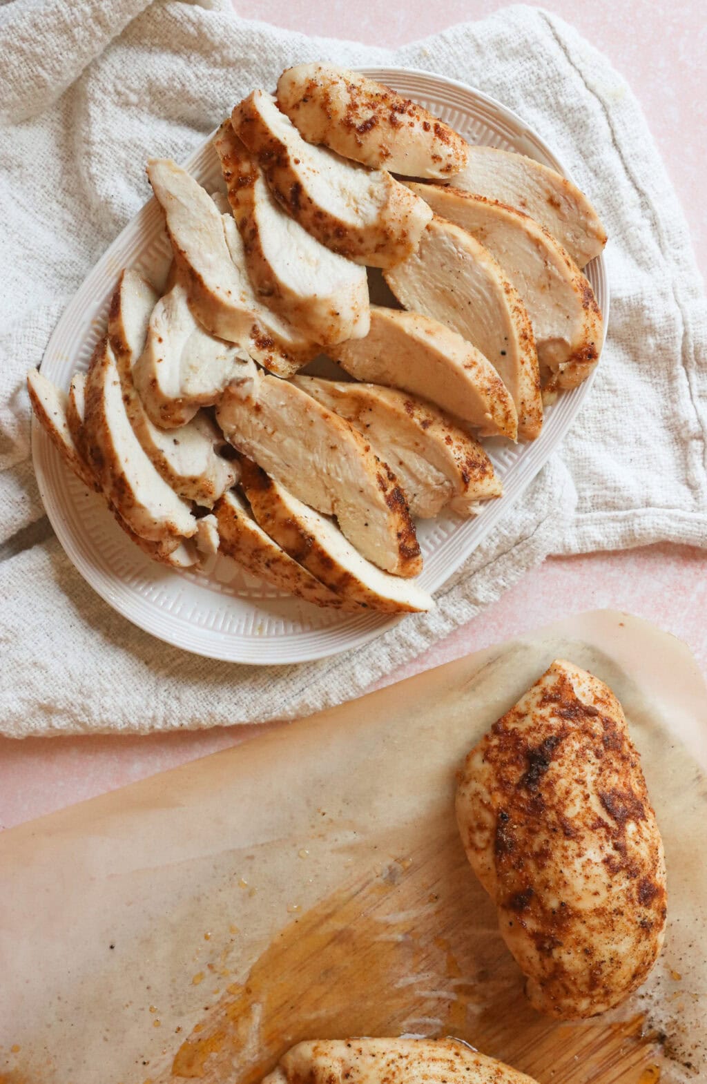 Cooked and sliced seasoned chicken breasts on a white serving dish with a white dish towel on the side