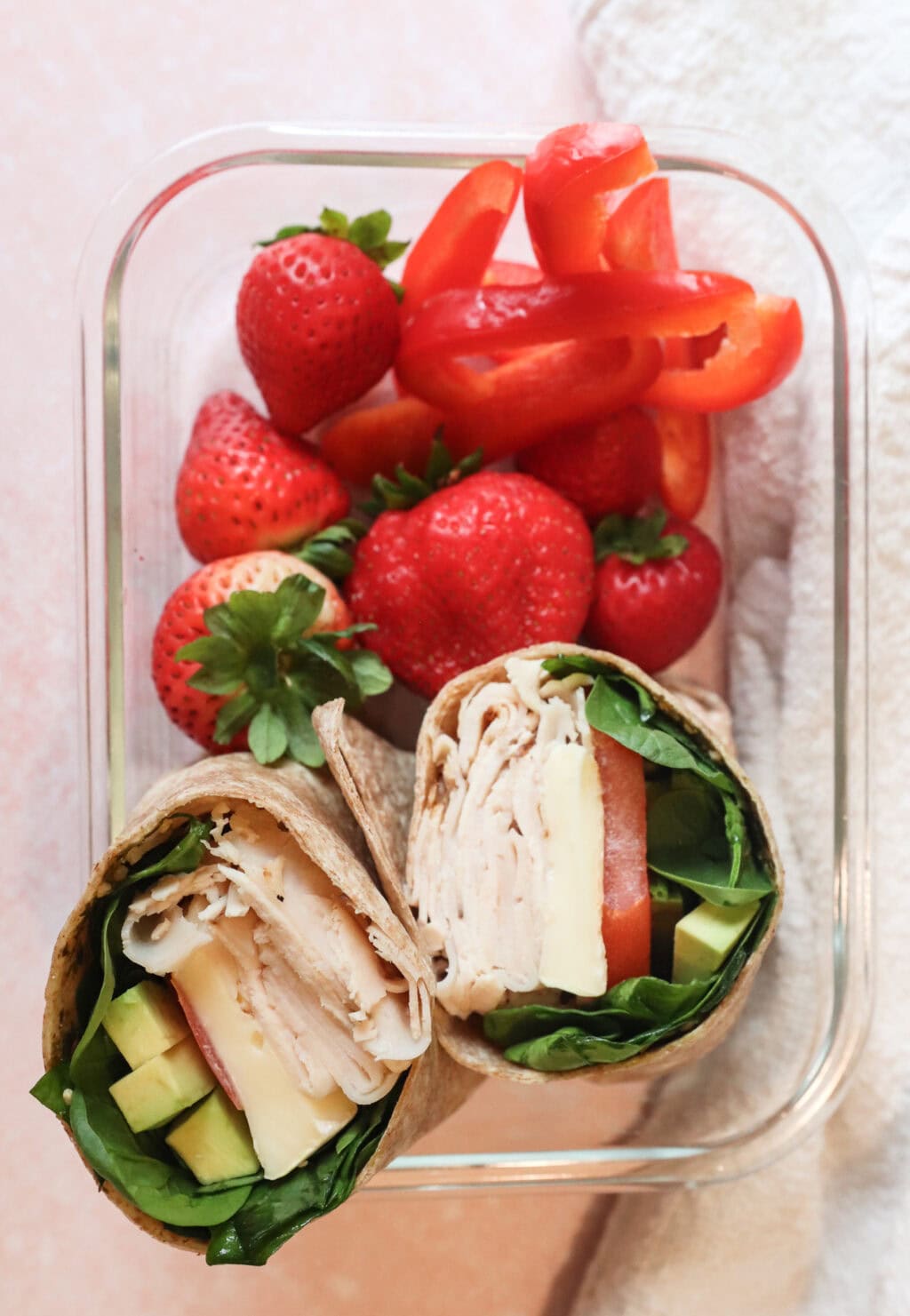 turkey pesto wrap, bundle with some strawberries and red bell peppers in a glass container the perfect lunch