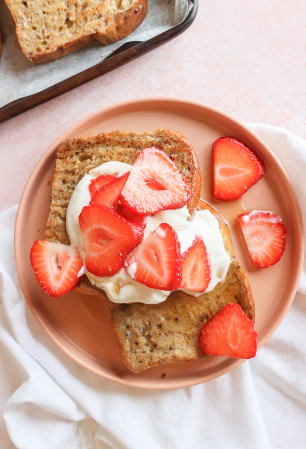 A plate of breakfast toast topped with Greek yogurt whipped cream and fresh strawberry slices, surrounded by a light, airy setup.