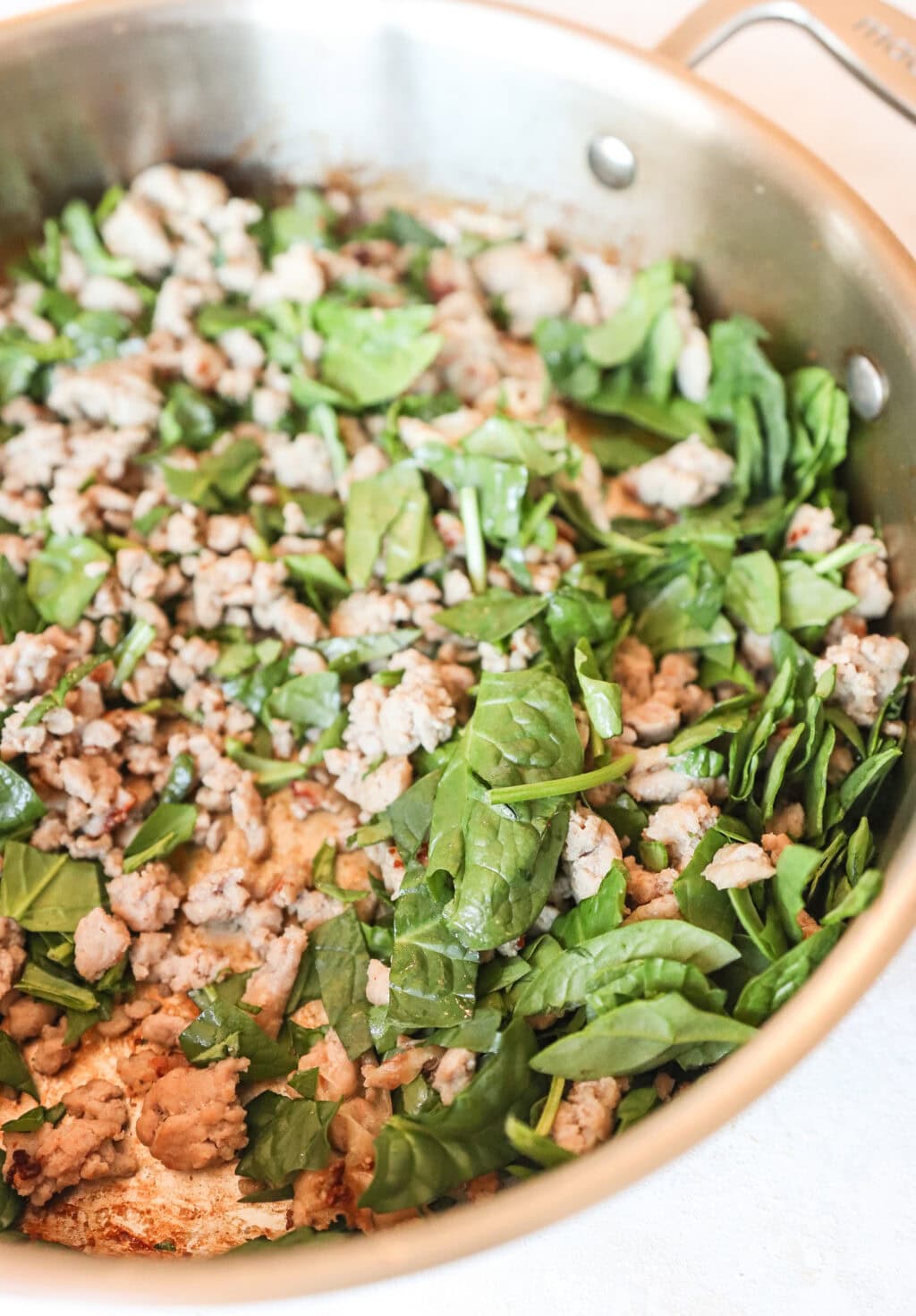 meat and spinach being cooked together in a frying pan