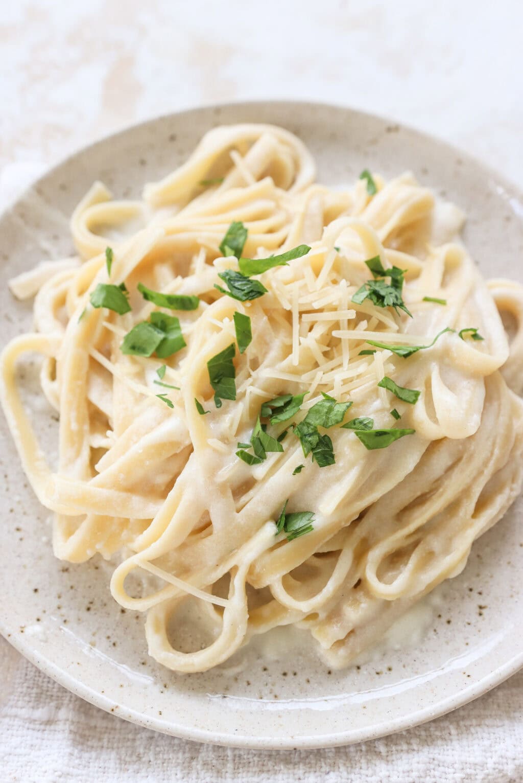 A plate of creamy cottage cheese Alfredo pasta garnished with fresh parsley and shredded Parmesan cheese, served on a light ceramic plate.