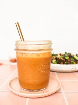 front view of the peanut lime dressing in a glass mason jar sitting on a pink plate on a pink counter top