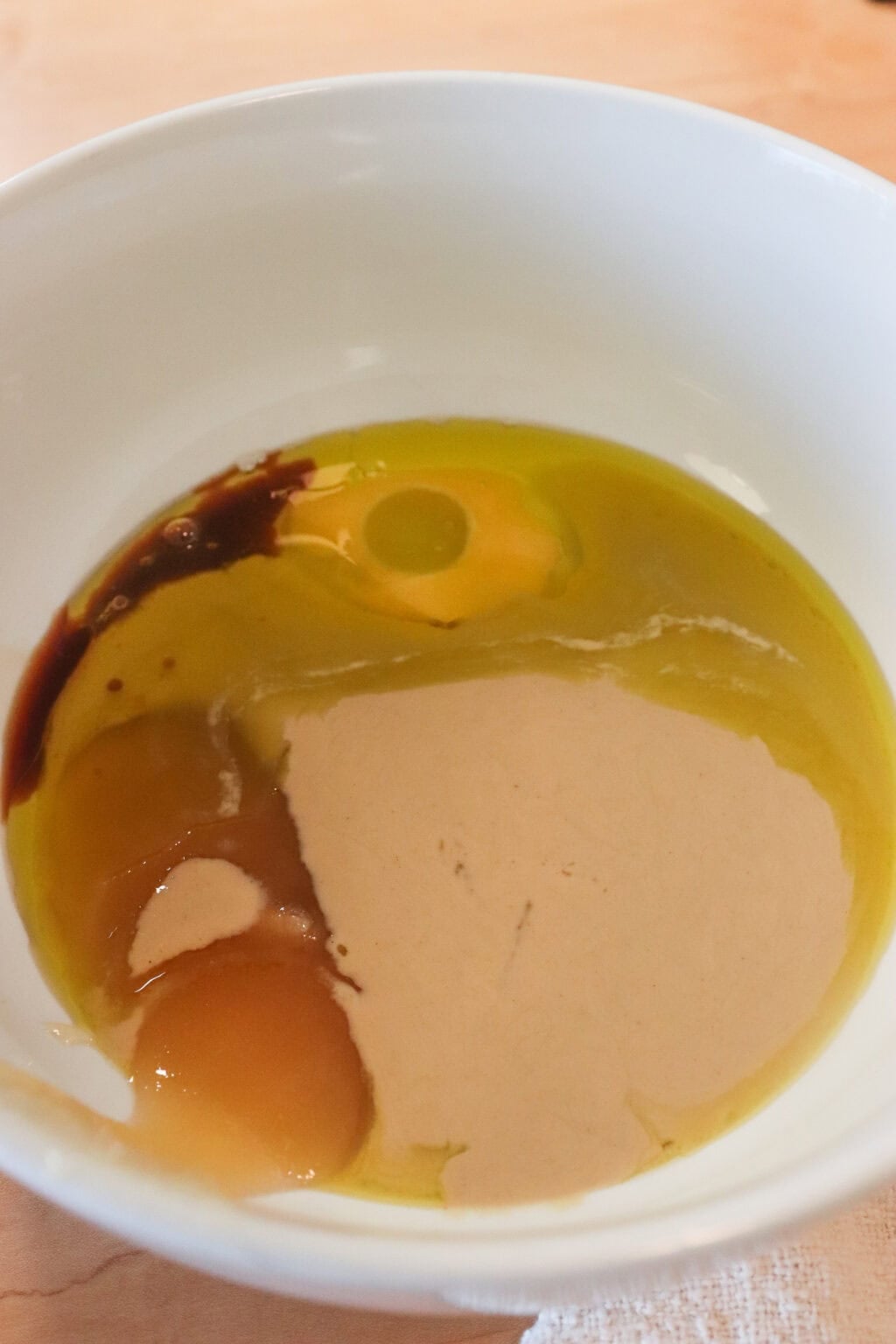 A bowl with a mix of wet ingredients like egg, vanilla, tahini, and honey for chewy healthy breakfast cookies.