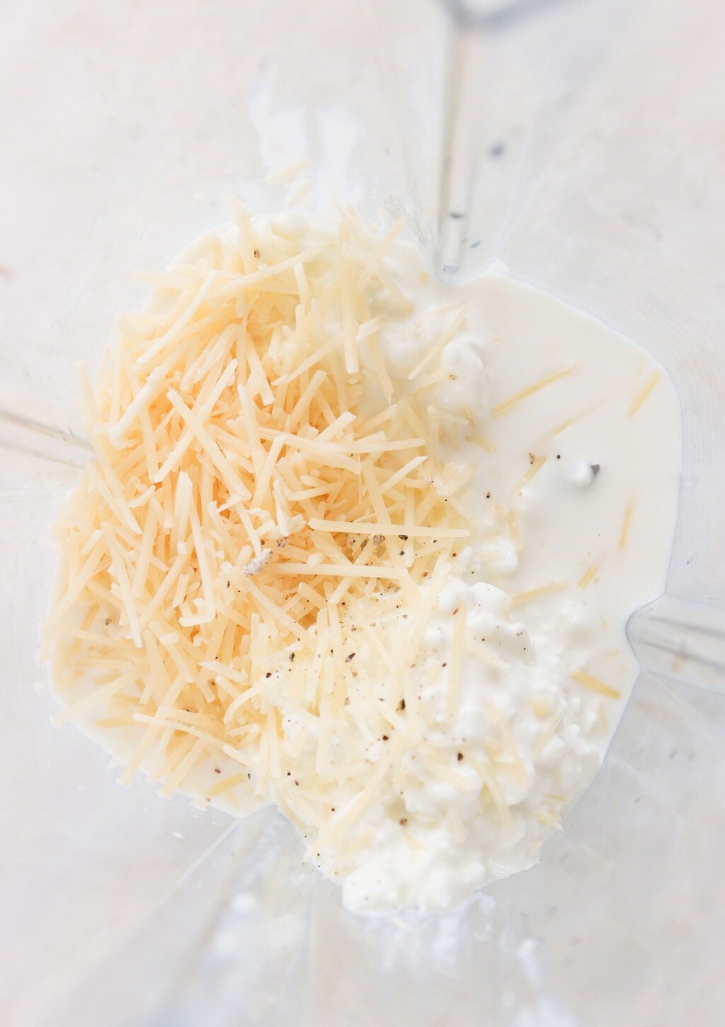 Cottage cheese, shredded Parmesan, milk, and pepper in a blender, ready to be blended into a smooth Alfredo sauce