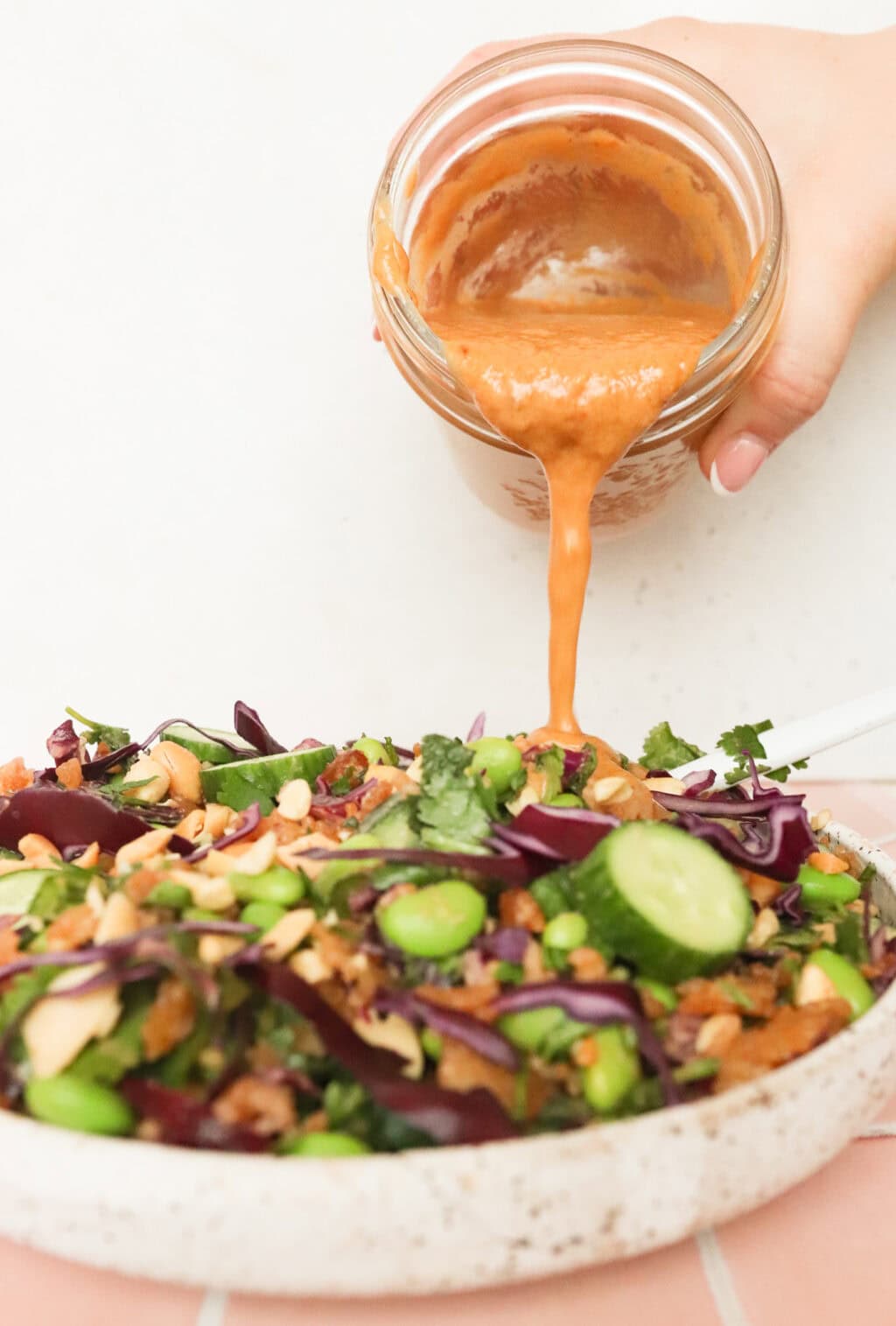 the peanut lime salad dressing being poured onto a beautiful green salad in a white bowl