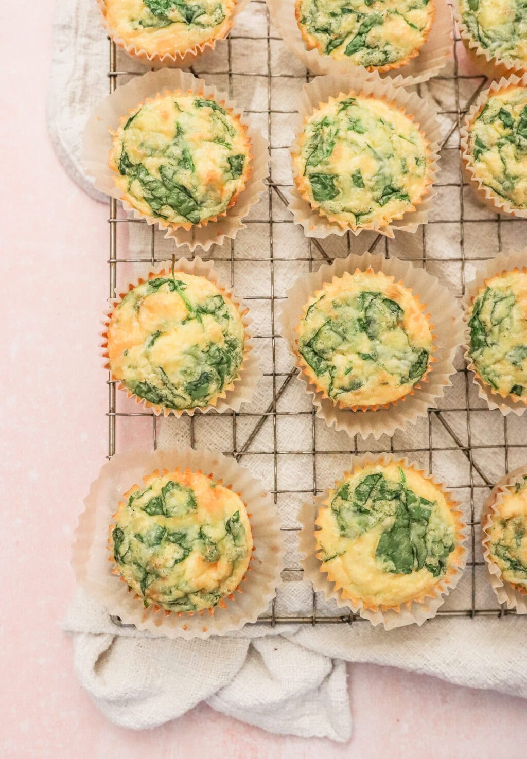 Freshly baked egg bites with spinach and cheese cooling on a wire rack lined with parchment paper.