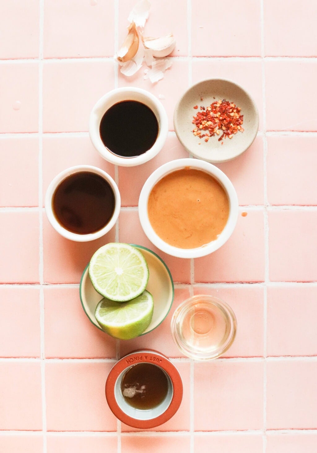 all the ingredients for the peanut lime dressing in small bowls on a pink countertop