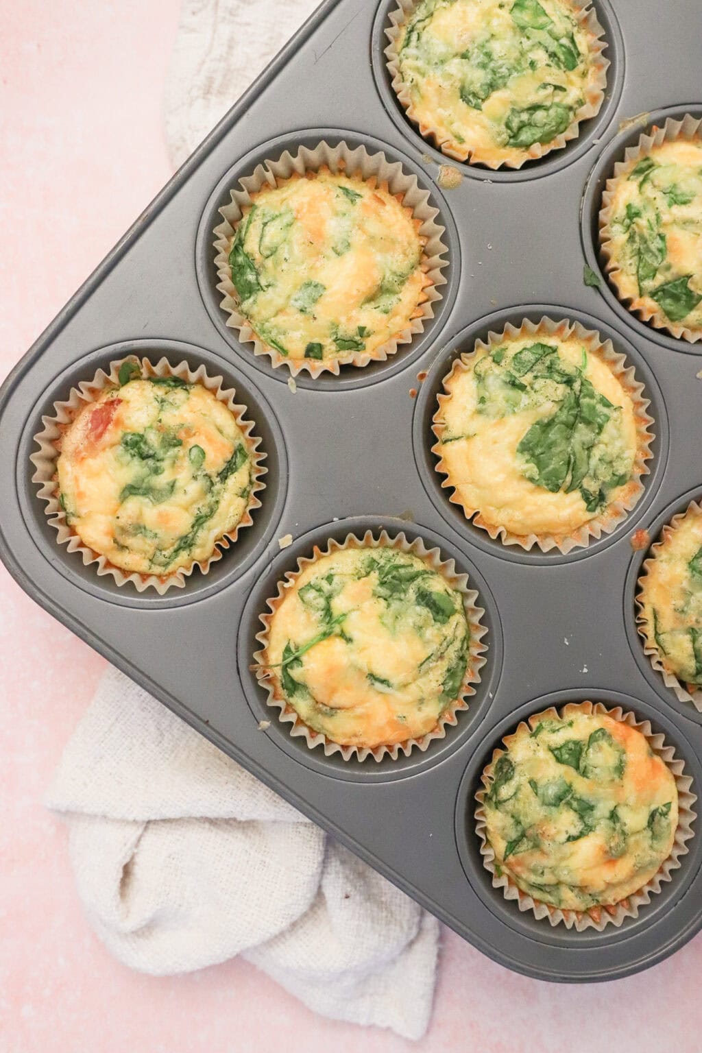 A muffin tray filled with golden-brown, spinach-filled egg bites, baked to perfection.