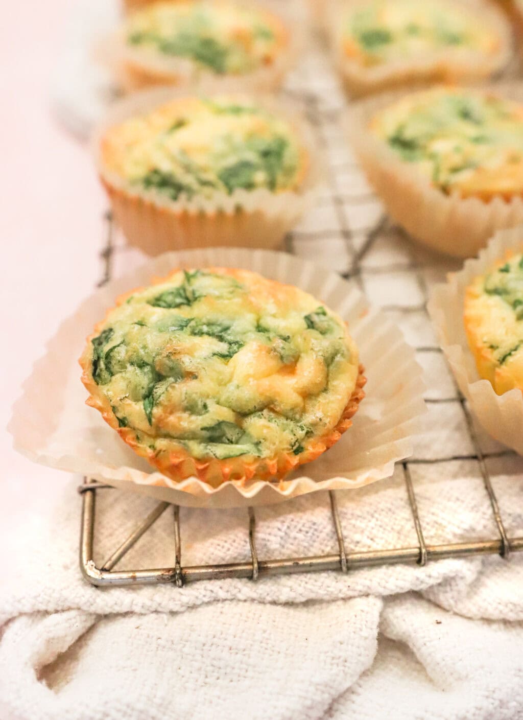 Freshly baked egg bites with spinach and cheese cooling on a wire rack lined with parchment paper.