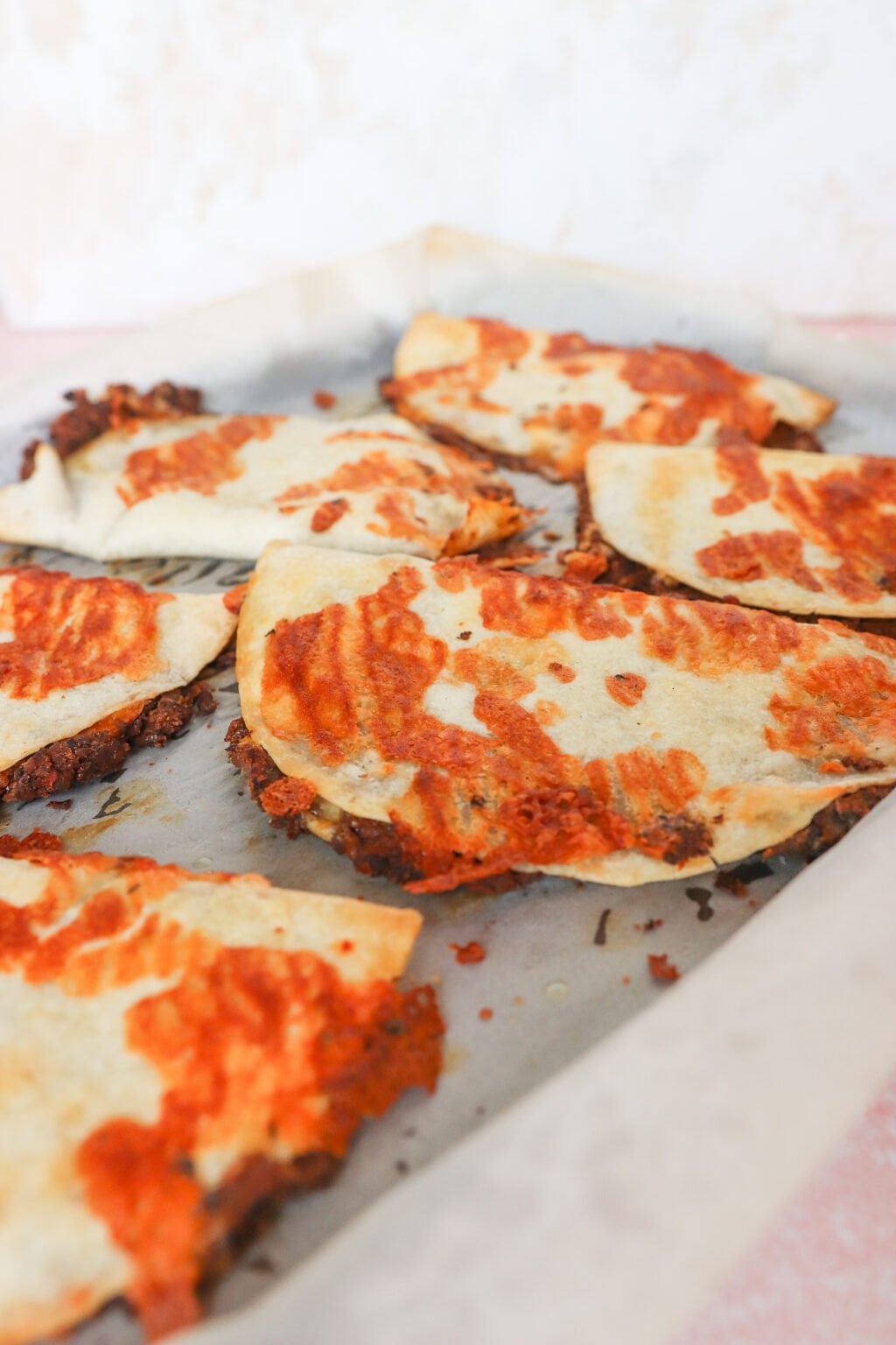 Close-up of fried tacos on a baking sheet lined with parchment paper. The tacos are golden with some browned spots, suggesting they were baked or fried to a crisp. The background is out of focus, emphasizing the tacos.