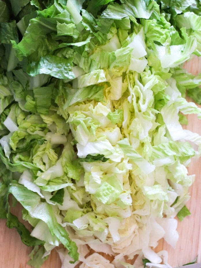 Chopped green lettuce leaves spread out on a light wooden surface, showing a mix of dark and light green to pale white colors.