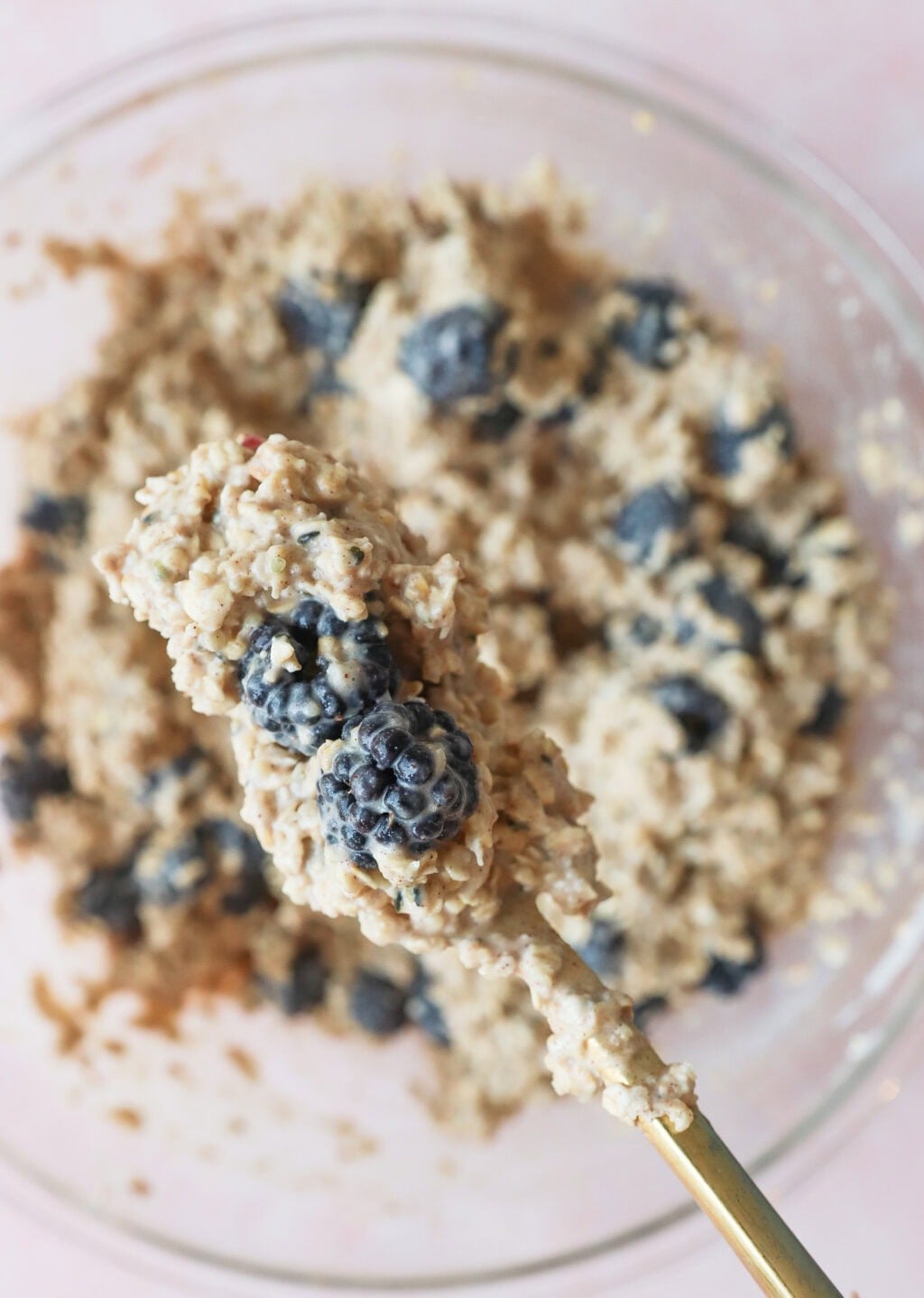 A close-up of a spoonful of oatmeal mixed with fresh blackberries, held above a glass bowl filled with the same blackberry oatmeal mixture.