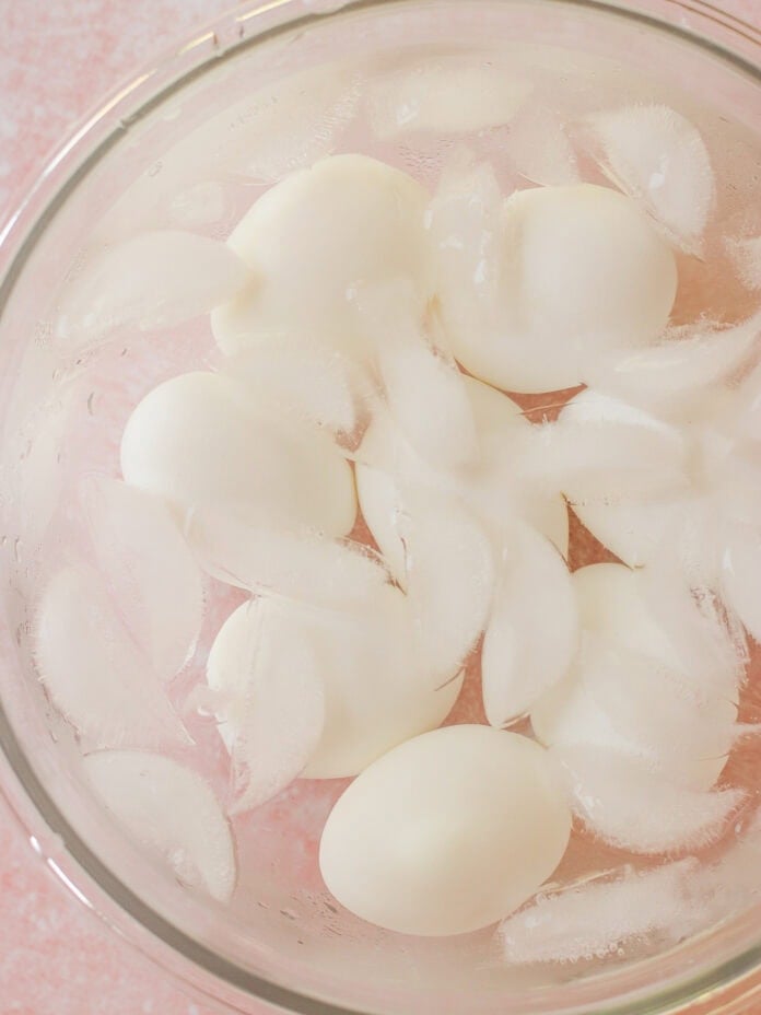 A glass bowl filled with hard-boiled eggs and ice cubes submerged in water, creating an ice bath.