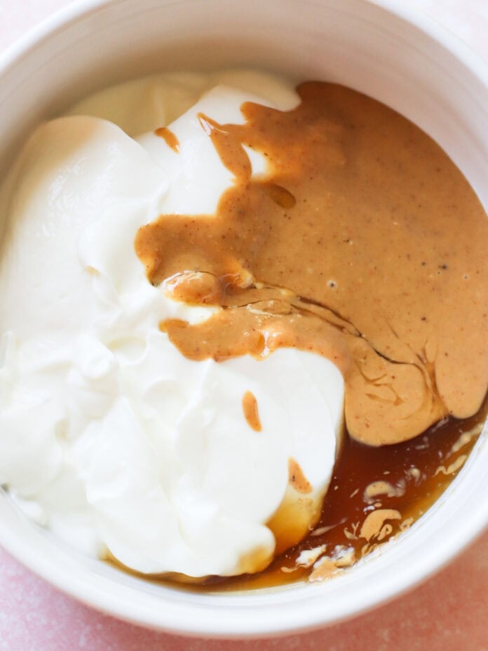 A white bowl filled with thick white yogurt, creamy brown peanut butter, and golden syrup, each ingredient slightly blending together but still distinct.