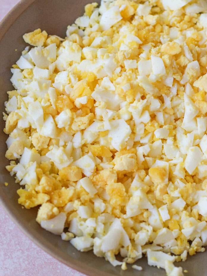 A close-up of a bowl filled with finely chopped hard-boiled eggs, showing a mix of yellow yolks and white egg whites.