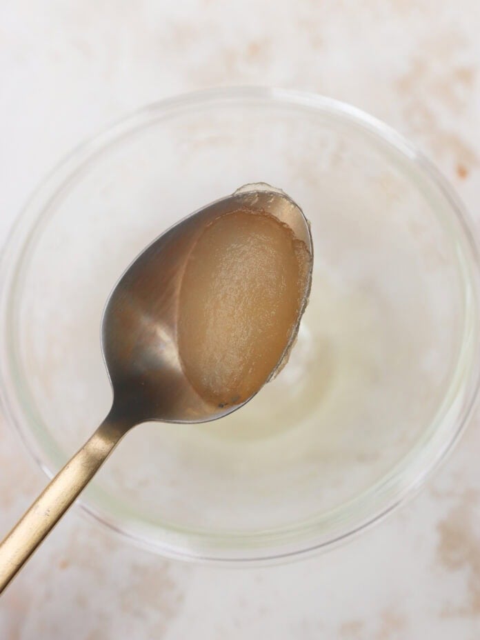 A spoon with a small amount of thick, translucent gel held over a clear glass bowl on a light-colored surface.