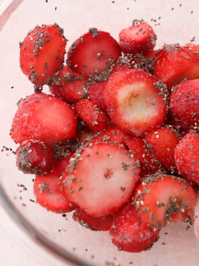 A glass bowl filled with sliced strawberries coated in chia seeds.