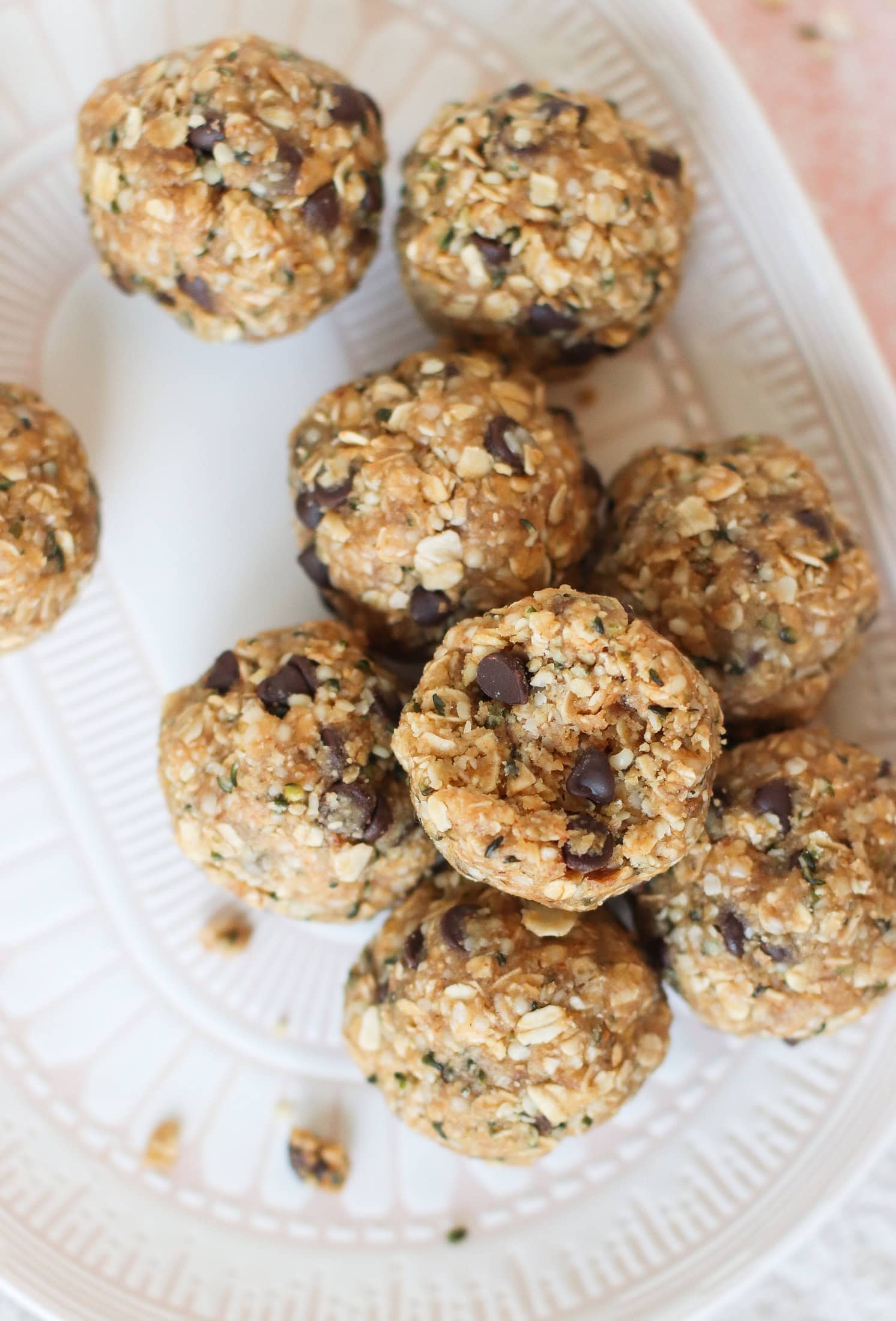 A close-up of round, homemade energy bites made with oats, chocolate chips, and seeds, arranged on a white patterned plate.