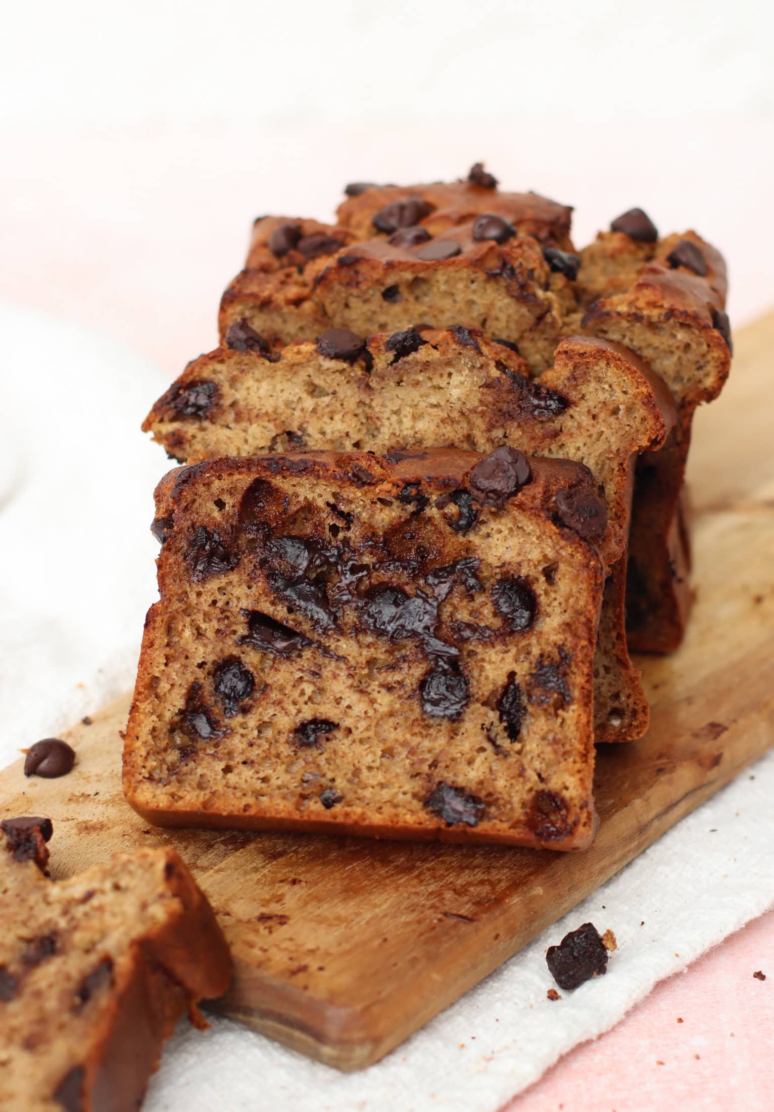 Sliced chocolate chip banana bread on a wooden board, showing moist texture and visible chocolate chips in each slice.