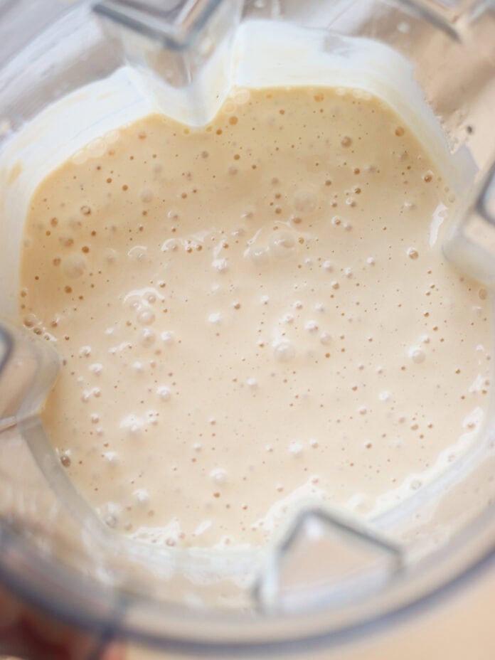 Creamy, lightly frothy batter or smoothie mixture in a blender, with small bubbles visible on the surface.