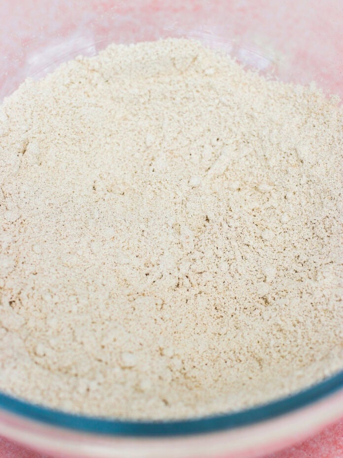 A glass bowl filled with light beige flour on a pink surface, showing a close-up of the fine, powdery texture—perfect for making fluffy Greek yogurt pancakes.